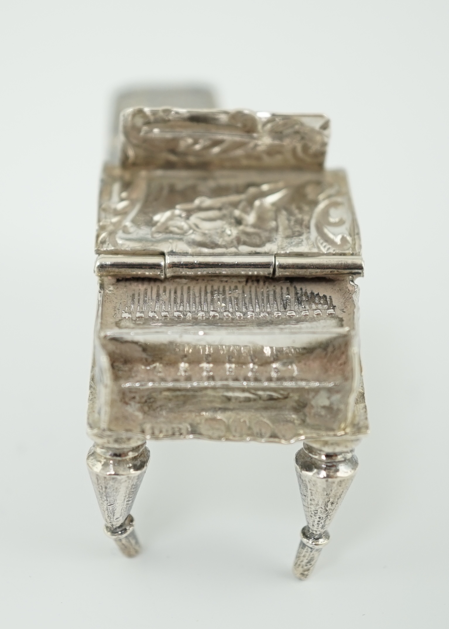 A late 19th century continental embossed silver miniature model of grand piano, length 53mm, together with a similar model of a table/desk on ornate scroll supports